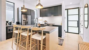 Une cuisine moderne avec des meubles de couleur sombre, un îlot central, des tabourets de bar et des luminaires suspendus.