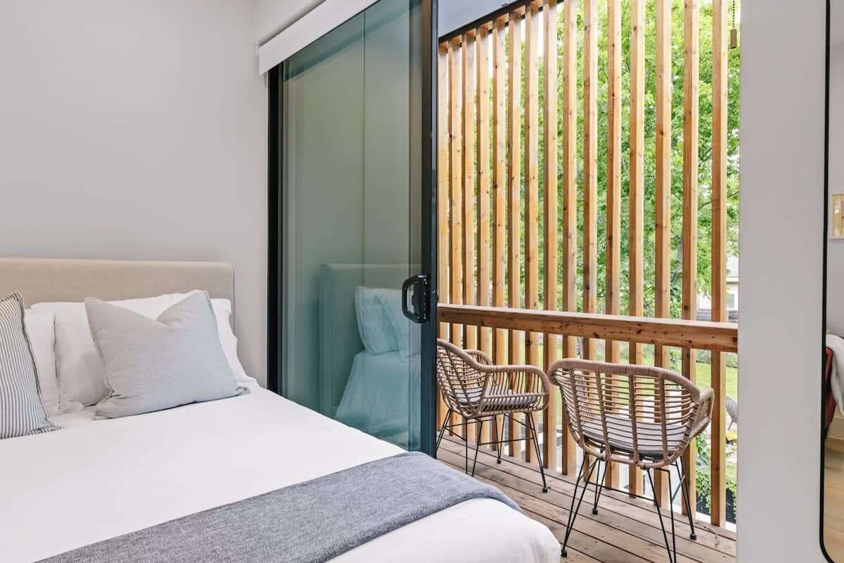 A bedroom with a bed, a sliding glass door, and a balcony with wicker chairs.