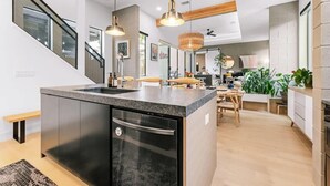 Une cuisine moderne dotée d’un îlot central, d’appareils électroménagers intégrés, de luminaires suspendus et d’un escalier avec des rampes en verre.