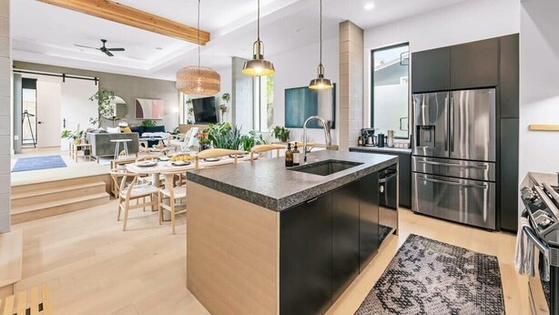 Une cuisine moderne dotée d’un îlot central, d’appareils électroménagers en acier inoxydable et de luminaires suspendus.