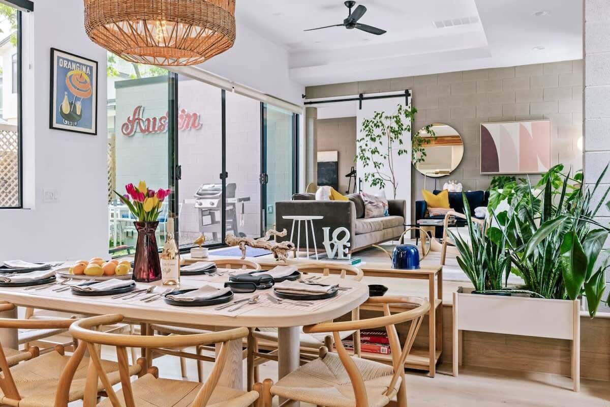 A modern living room with a dining area, large windows, and indoor plants.