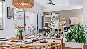 Un salon moderne avec un coin repas, de grandes fenêtres et des plantes d’intérieur.
