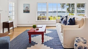 A living room with a large window, a red coffee table, a beige sofa, and a decorative vase. - Minutes from Downtown Easton and St. Michaels | Pool | Private Dock (Easton)