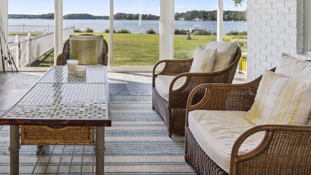 A covered patio with wicker furniture, a table, and a view of a lake and grassy area. - Minutes from Downtown Easton and St. Michaels | Pool | Private Dock (Easton)