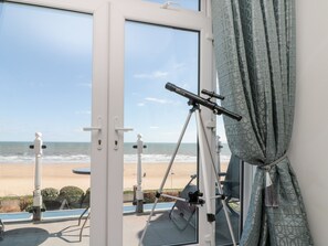 A room with a telescope on a tripod, a beach view through a glass door, and a patterned curtain. - Crystal Cove (Bridlington)