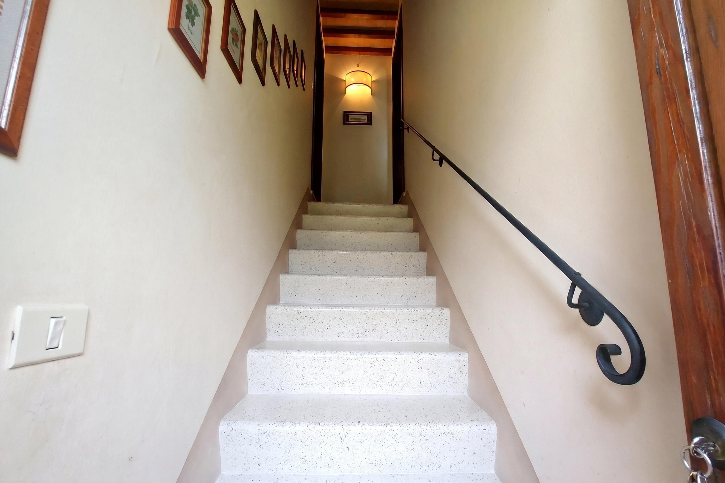 Un escalier avec une rampe, un luminaire en haut et des tableaux encadrés accrochés au mur.