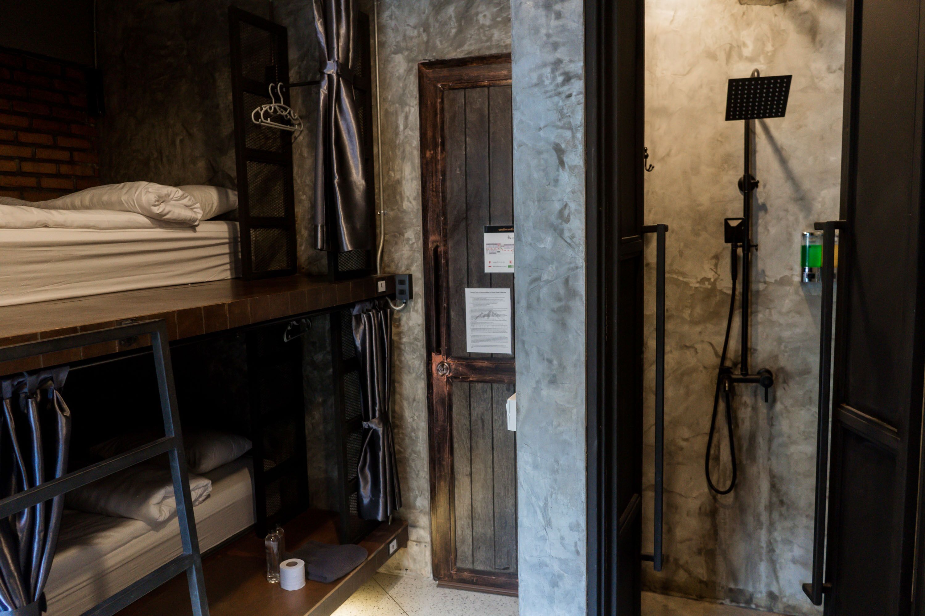 A dormitory room with bunk beds, a shower, and a door with a notice.