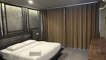 Une chambre moderne avec un grand lit, une tête de lit au motif texturé, une table de chevet avec une lampe et une fenêtre donnant sur l’extérieur.