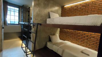 A compact room with bunk beds, a ladder, a window with curtains, and a brick-patterned wall.