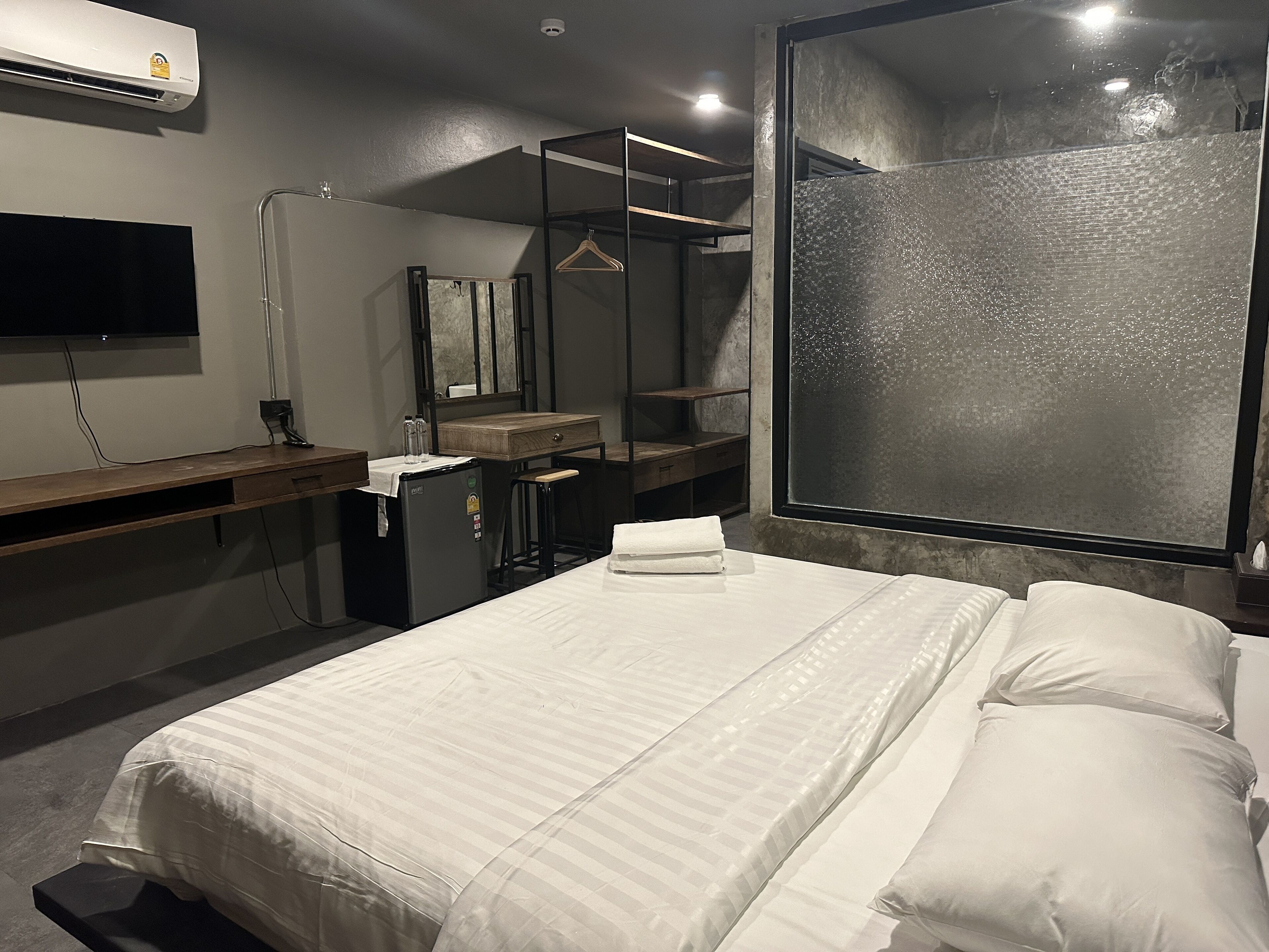 Une chambre d’hôtel avec un lit, un bureau doté d’un miroir, un petit réfrigérateur et une grande fenêtre offrant une vue intéressante.