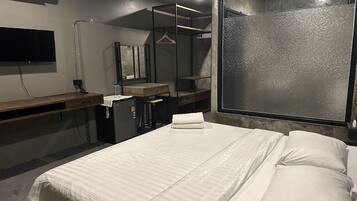 Une chambre d’hôtel avec un lit, un bureau doté d’un miroir, un petit réfrigérateur et une grande fenêtre offrant une vue intéressante.