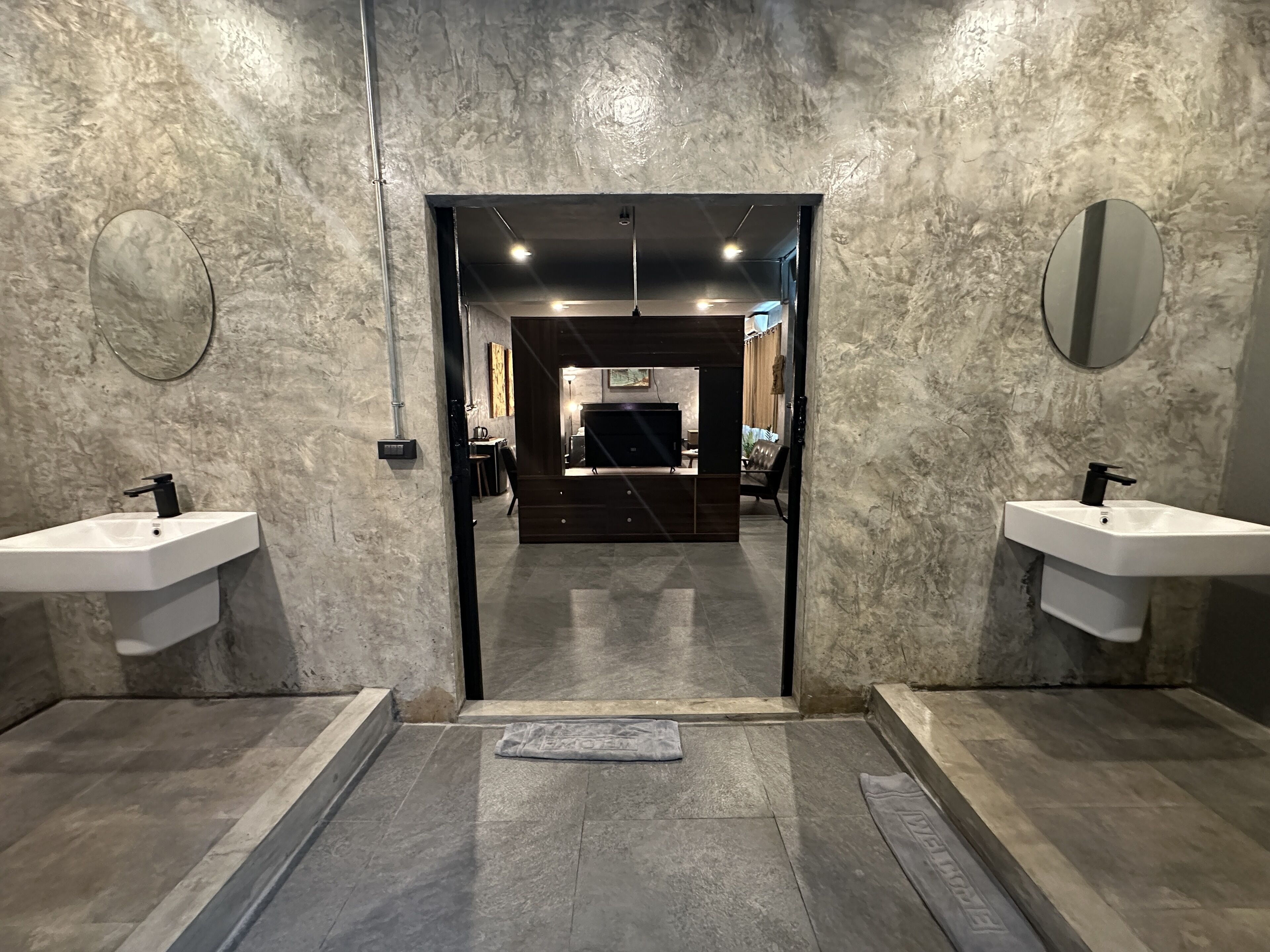 A modern bathroom with two sinks, a mirror, and a door leading to a living area.