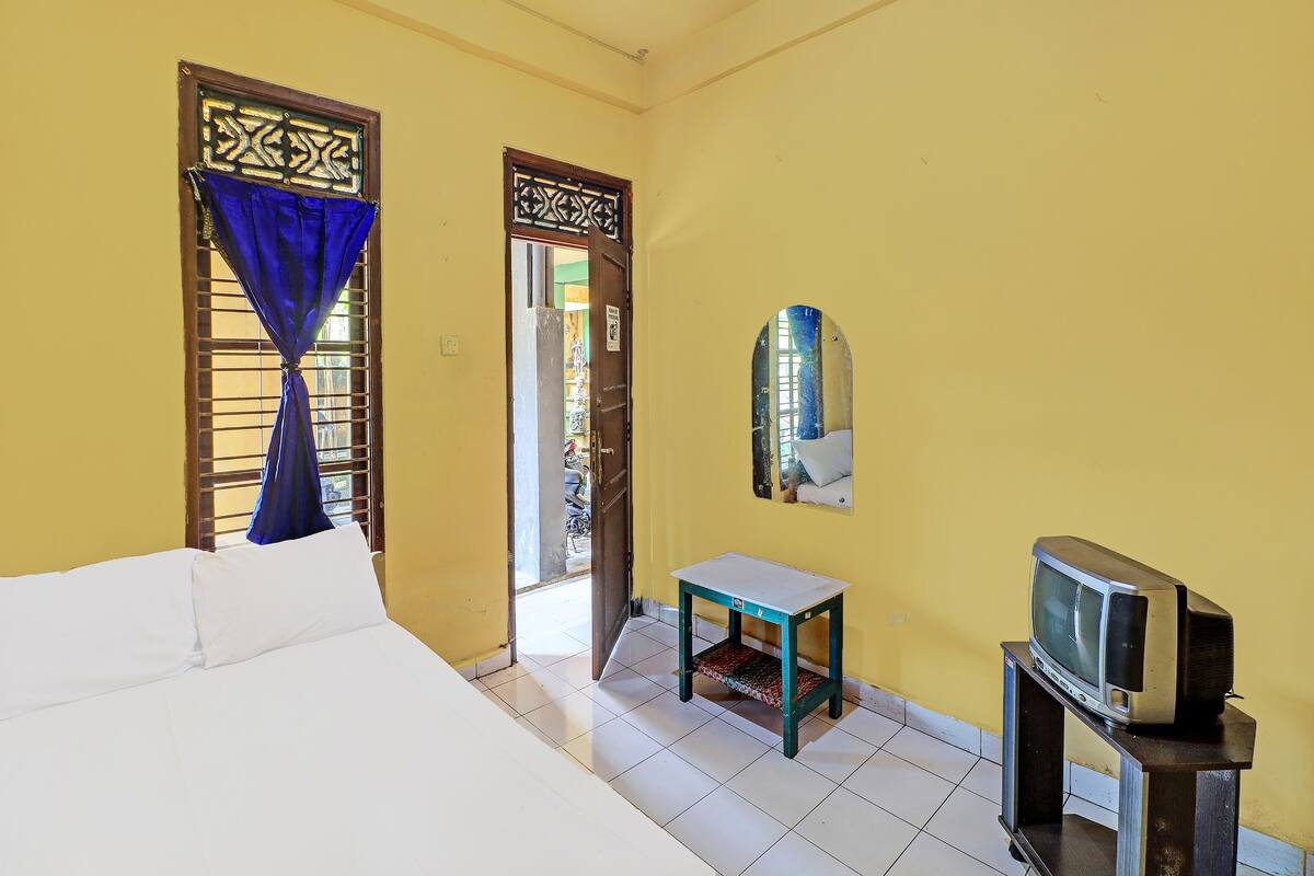 Una habitación con una cama, una mesita, un televisor sobre un mueble bajo y un espejo en la pared.