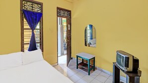A room with a bed, a small table, a television on a stand, and a mirror on the wall. - OYO 91235 Pondok Damu (Mengwi)