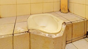 A corner of a bathroom with a toilet, tiled walls, and a yellow pipe. - OYO 91235 Pondok Damu (Mengwi)