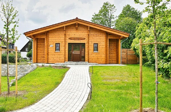 A wooden cabin with a paved entrance, surrounded by greenery and trees. - Doppelhaushälfte in Hasselfelde (Hasselfelde)