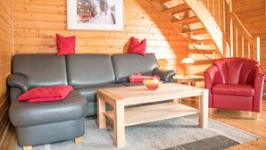Een gezellig houten interieur van een blokhut met een bank, een rode fauteuil, een houten bijzettafeltje en een trap.