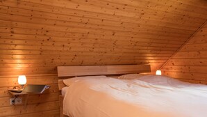 Een houten slaapkamer met een enkel bed, een nachtkastje met een lamp en een wandplank.