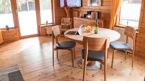 Een gezellig houten blokhut met een ronde eettafel, vier stoelen, een laptop en een aan de muur bevestigde televisie.