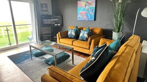 Uma sala de estar moderna com um sofá amarelo, uma mesa de centro de vidro e uma janela grande.