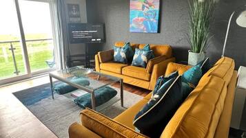 A modern living room with a yellow sofa, a glass coffee table, and a large window.