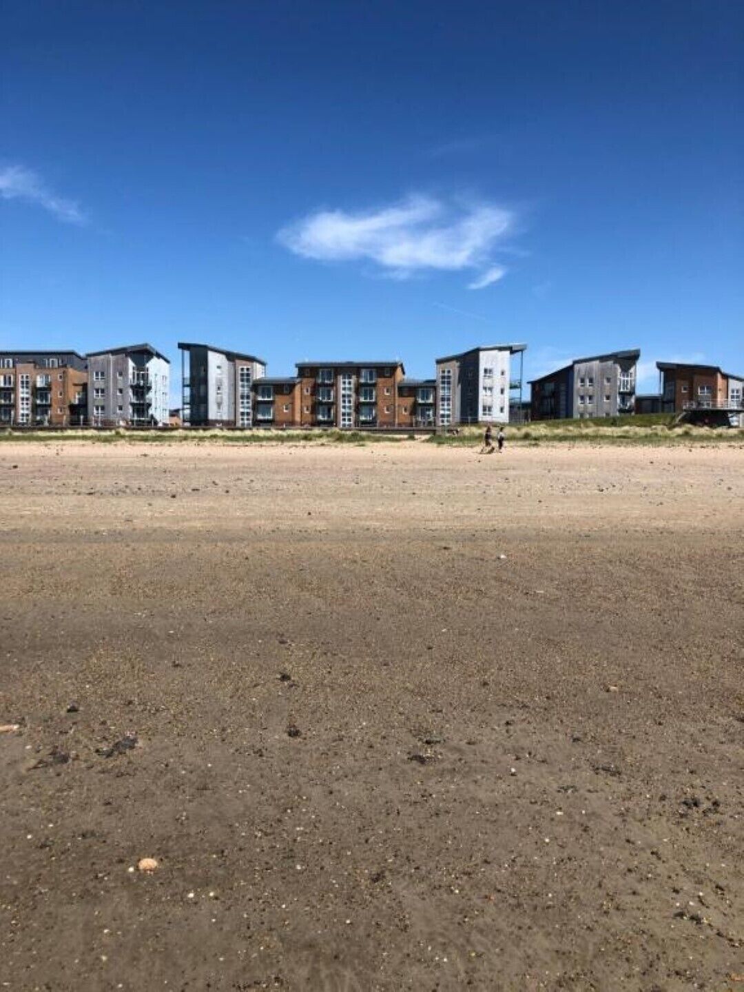 A row of modern multi-story buildings with a sandy foreground, likely a beach or coastal area.