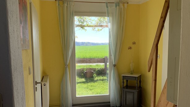 A room with a view of a green field through a window with curtains.