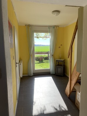 A room with a view of a green field through a window with curtains.