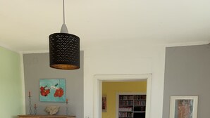 A bedroom with a bed, a wooden wardrobe, a bookshelf, and a hanging light fixture.