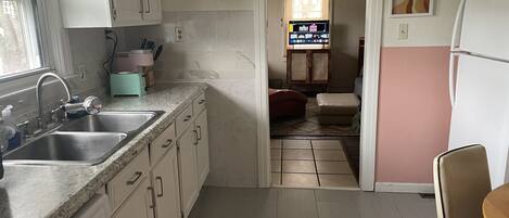 A kitchen with white cabinets, a granite countertop, a sink, and a toaster. There is a rug on the floor and a chair in the dining area.