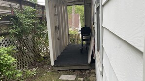 Un espacio exterior techado con un sendero de hormigón que lleva a una puerta, rodeado de una valla de madera y vegetación.