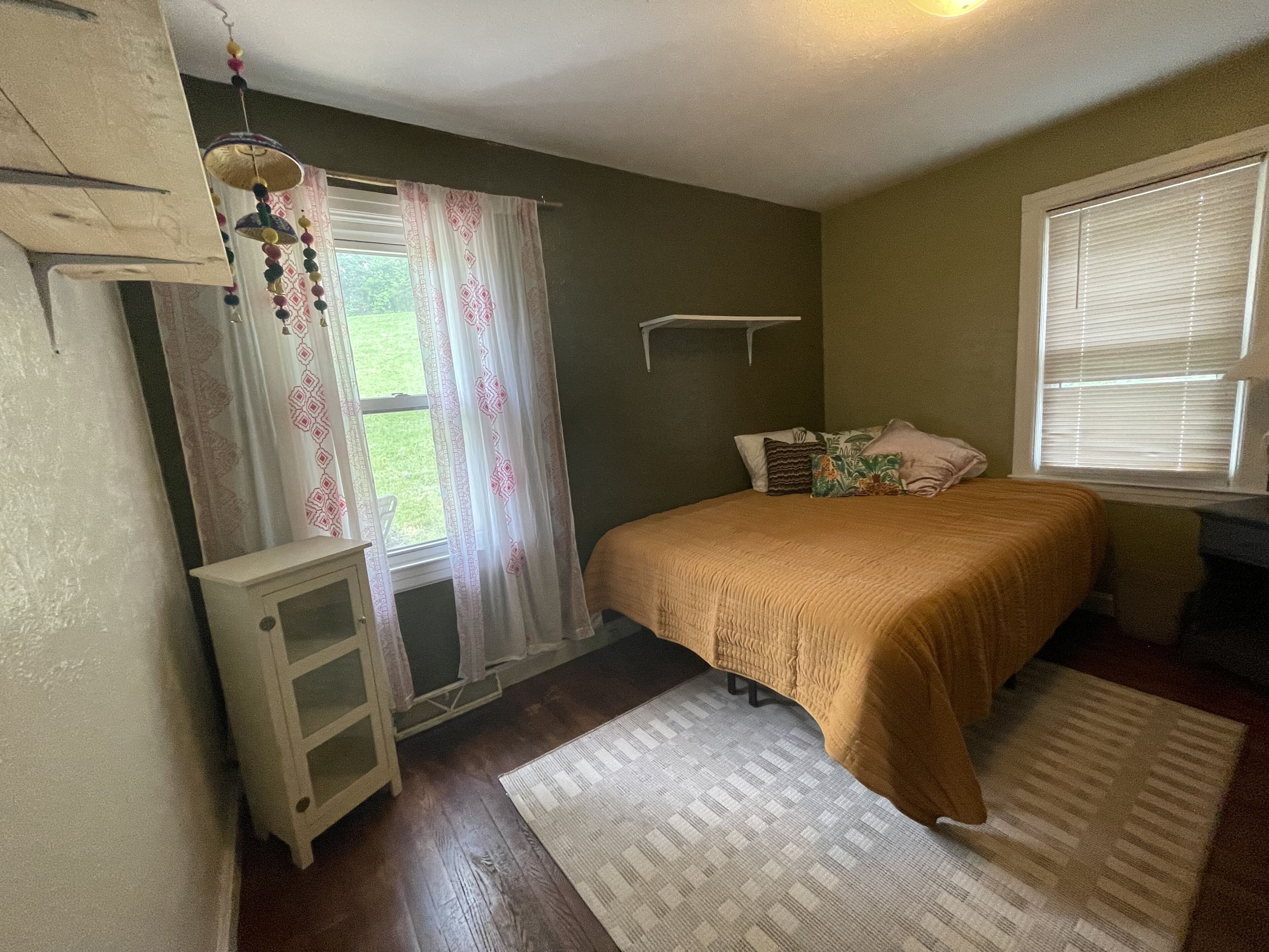 A bedroom with a bed, a nightstand, a dresser, a window with curtains, and a ceiling fan.
