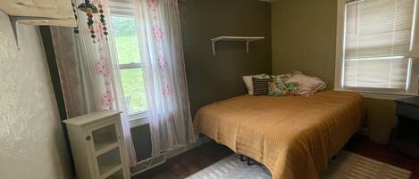 A bedroom with a bed, a nightstand, a dresser, a window with curtains, and a ceiling fan.