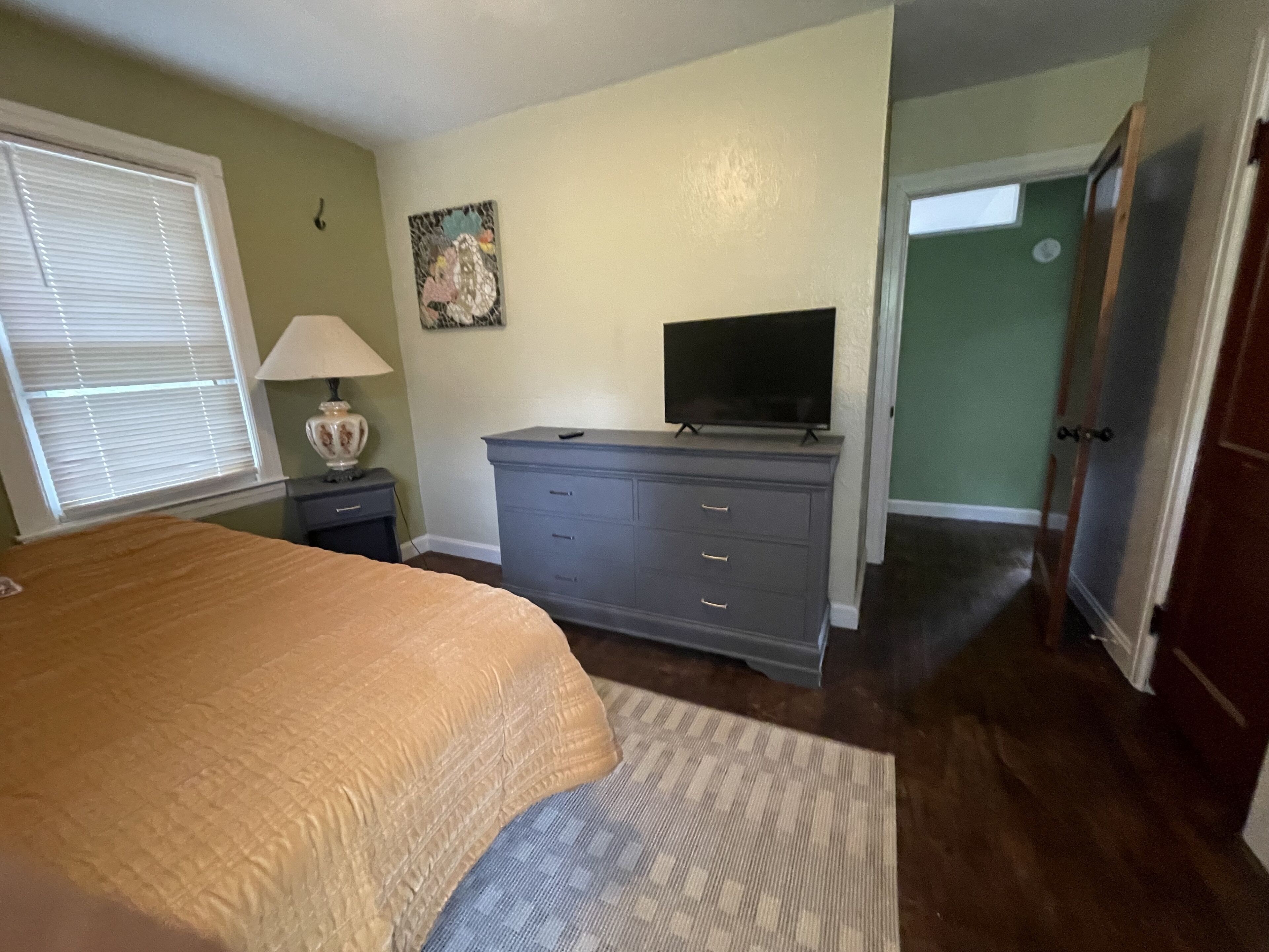 Une chambre à coucher avec un lit, une commode, une télévision, une lampe et un tableau au mur.