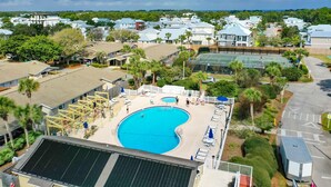 Zona residencial con una gran piscina rodeada de casas, palmeras y una cancha de tenis.
