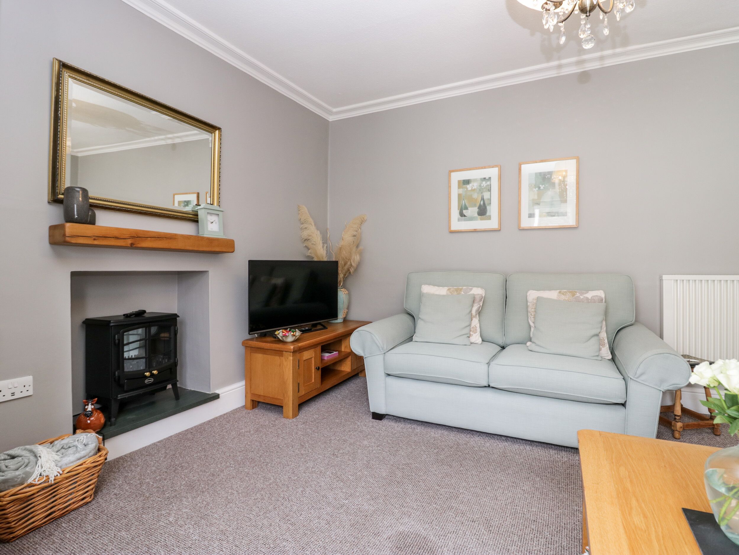 A living room with a grey sofa, a television on a wooden stand, a fireplace, and a chandelier.