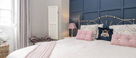 A bedroom with a bed, a nightstand, a lamp, a radiator, and a window with curtains.