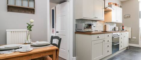 A modern kitchen with white cabinets, a microwave, and a stove. There is a dining table with plates and a vase of flowers.
