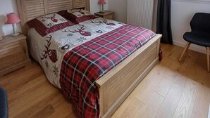 Ein Schlafzimmer mit einem hölzernen Bett, einem Nachttisch mit Lampe, einem Fenster mit Vorhängen und einem Sessel.