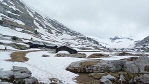 Eine Berglandschaft mit verschneitem Boden, felsigem Gelände und einigen Holzbauten.