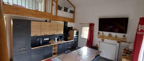 A modern kitchen with wooden cabinets, a dining table, and chairs. There is a staircase leading to an upper level.