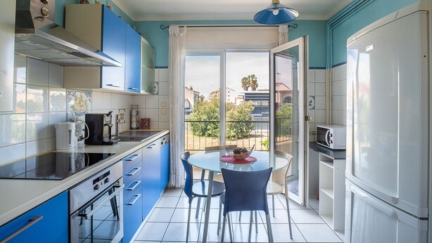A compact kitchen with blue cabinets, a dining area with a table and chairs, and a view through the open door.