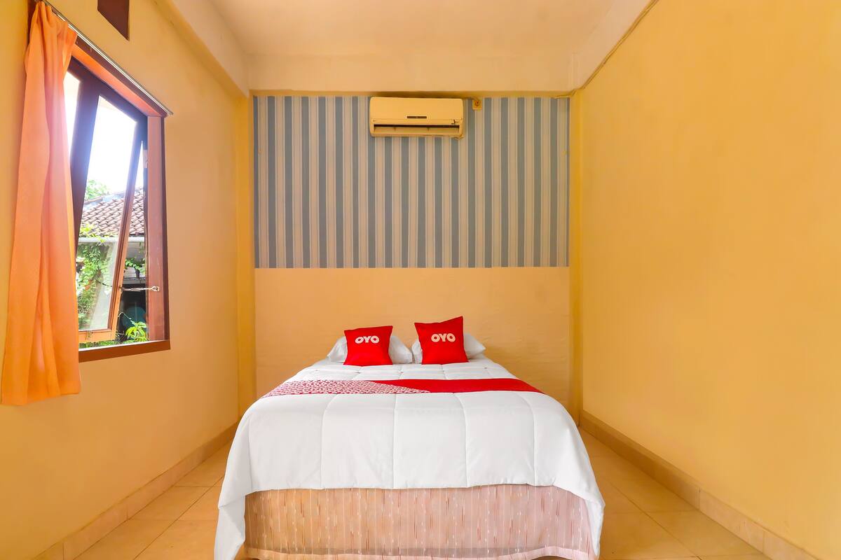 A hotel room with a bed, a window with curtains, a striped wall, and an air conditioning unit.