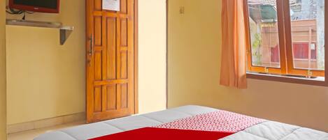 A hotel room with a bed, a wooden door, a television, and a window with curtains.