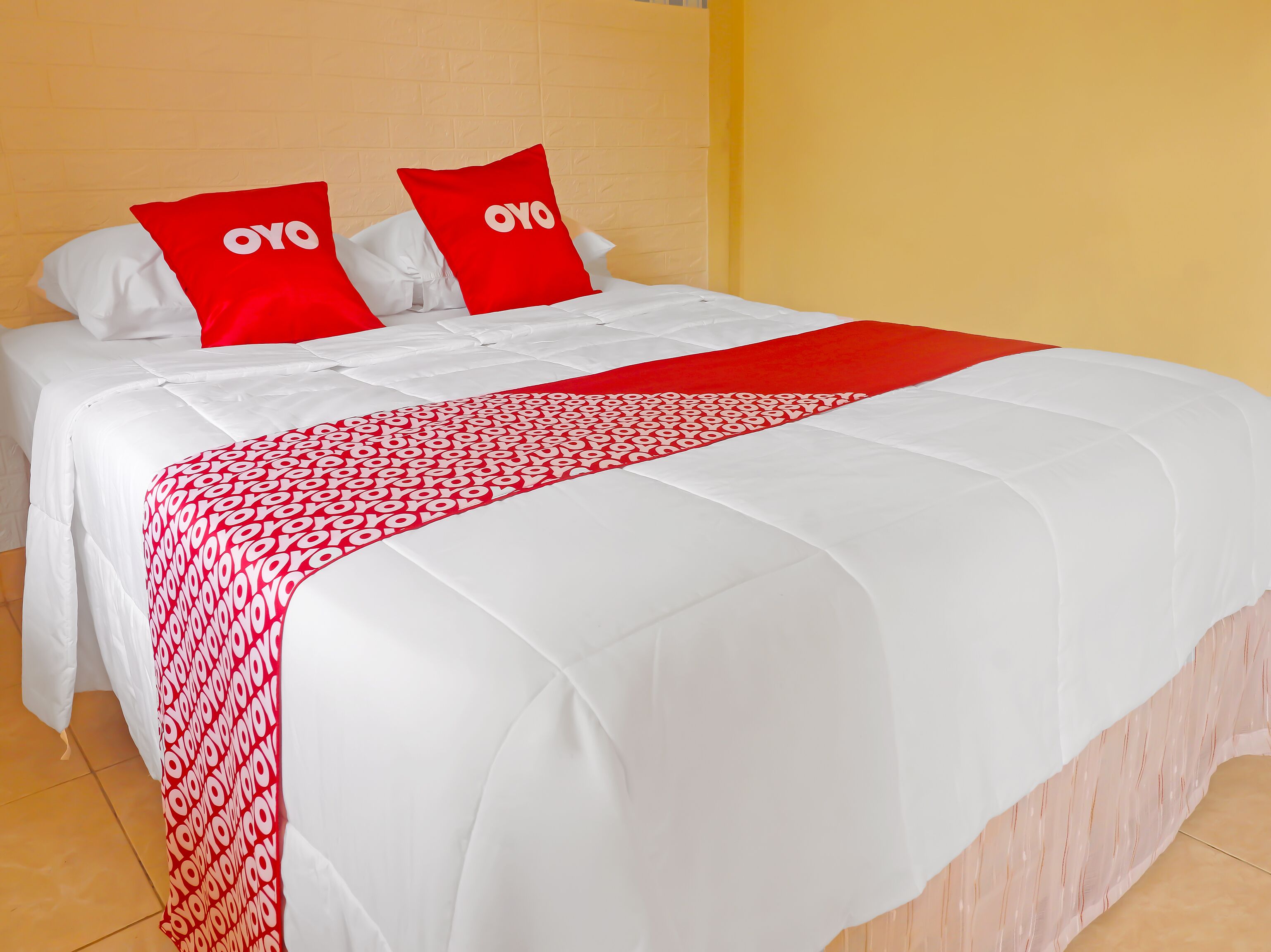 Una cama con ropa de cama blanca y detalles en rojo, incluyendo almohadas y una colcha.