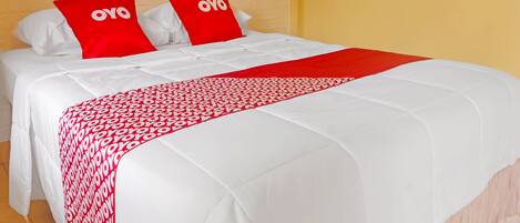 Una cama con ropa de cama blanca y detalles en rojo, incluyendo almohadas y una colcha.
