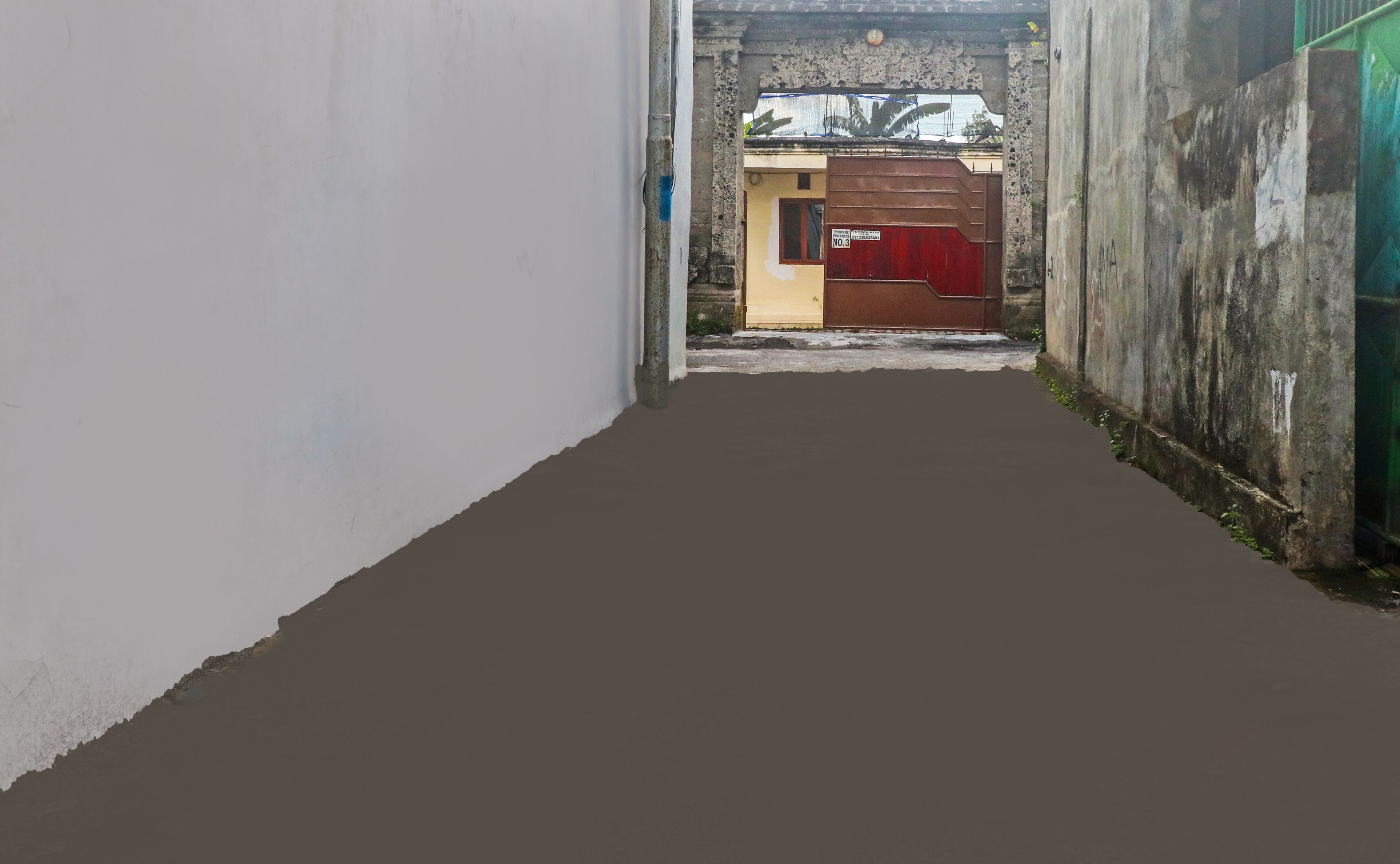 A narrow alleyway with a concrete floor, a yellow door with a red curtain, and a green gate on the right.