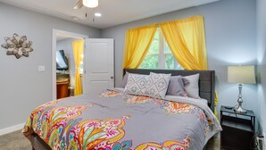 Quarto com cama, ventoinha no teto, mesa de cabeceira e janela com cortinas amarelas.