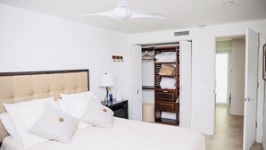 Ein Hotelzimmer mit Bett, Nachttisch, Deckenventilator, Kleiderschrank und einer offenen Tür zu einem anderen Raum.