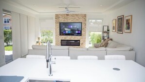 Ein modernes Wohnzimmer mit Flachbildfernseher an einer Steinwand, einer Couch und einem Essbereich mit weißem Tisch und Stühlen.